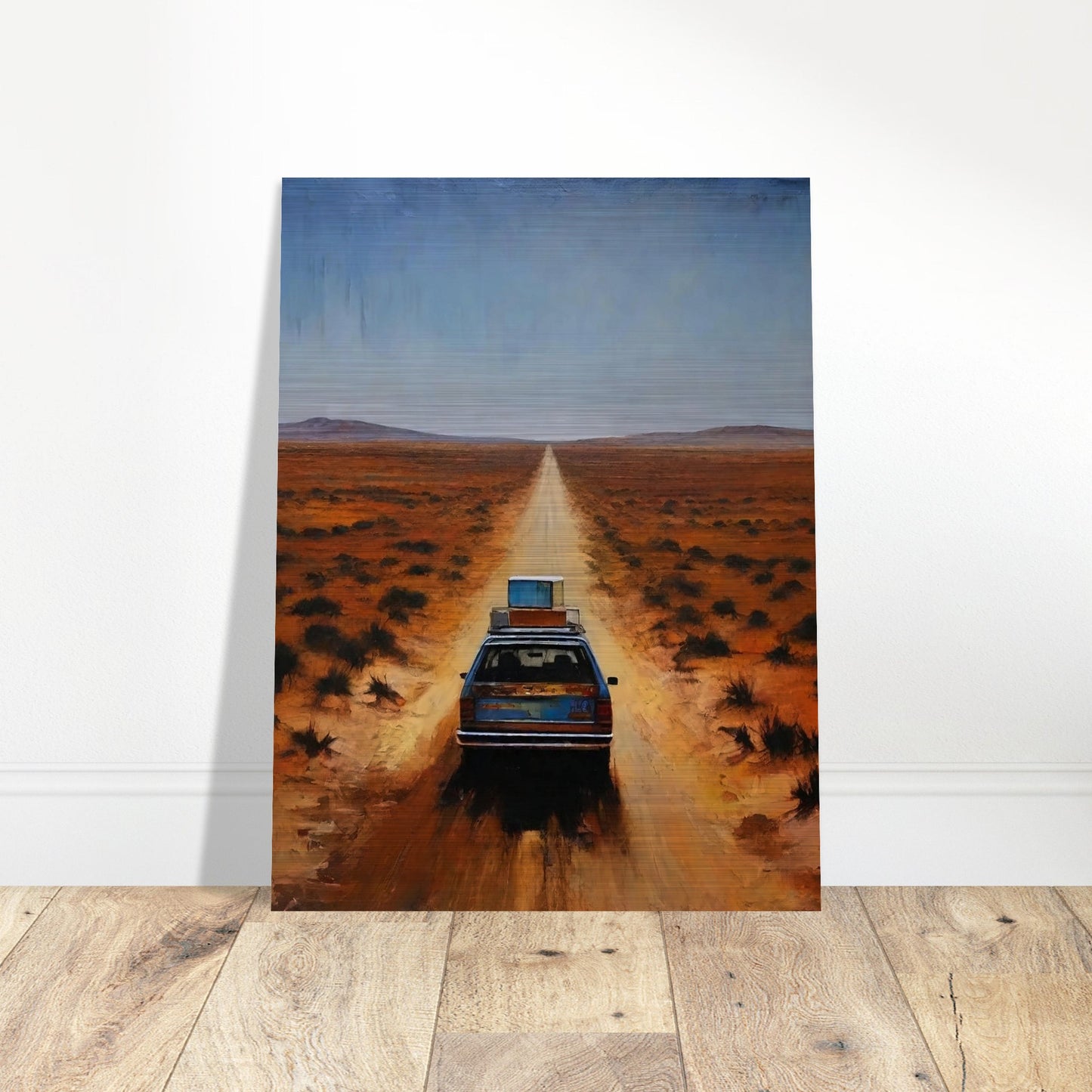 A car driving down a long, desolate road in a vast desert landscape under a clear blue sky.