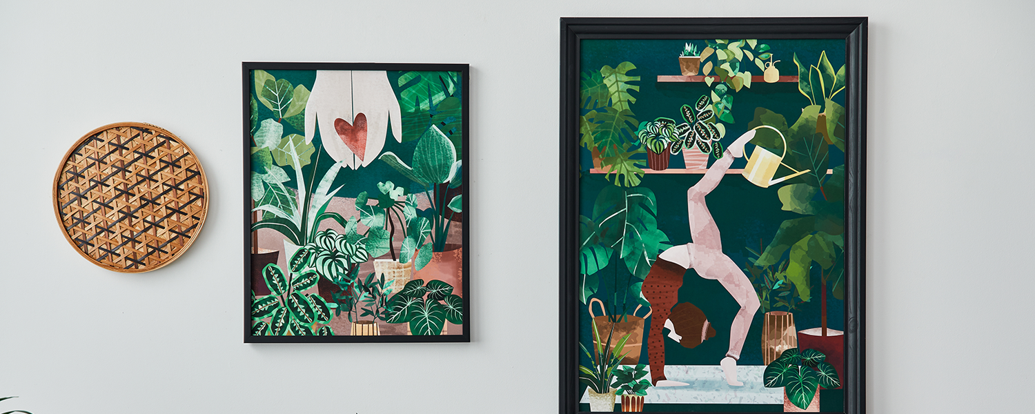 Two framed botanical and yoga-themed artworks on a wall above a wooden table filled with potted plants, creating a natural and serene home decor setup.