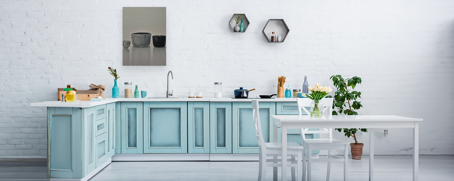Bright kitchen with pastel blue cabinets, a minimalist white dining table, and a wall art piece featuring ceramic bowls in neutral tones displayed above the countertop.