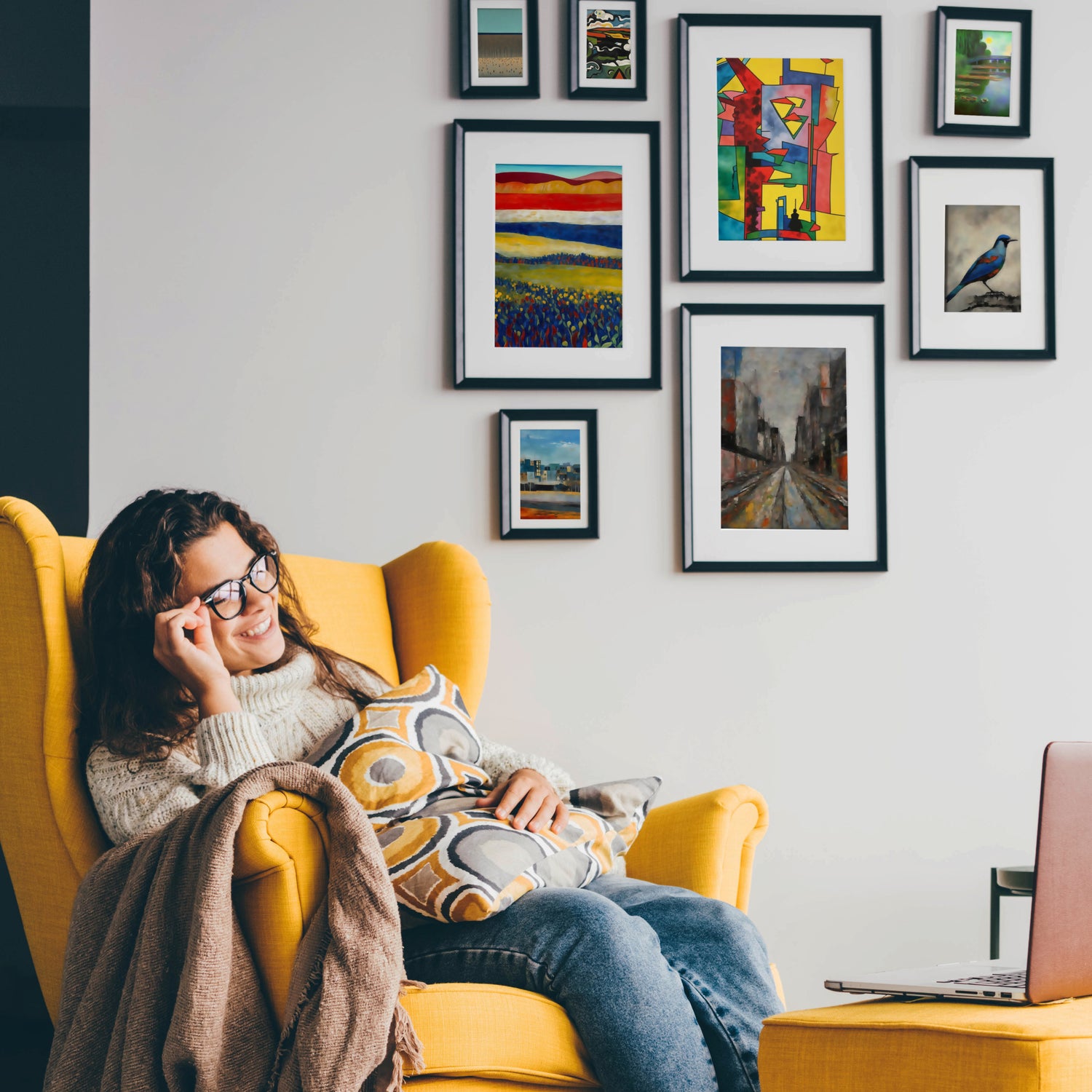 Smiling woman sitting in a yellow armchair with colorful gallery wall in the background, showcasing various framed artwork, adding warmth to the room.