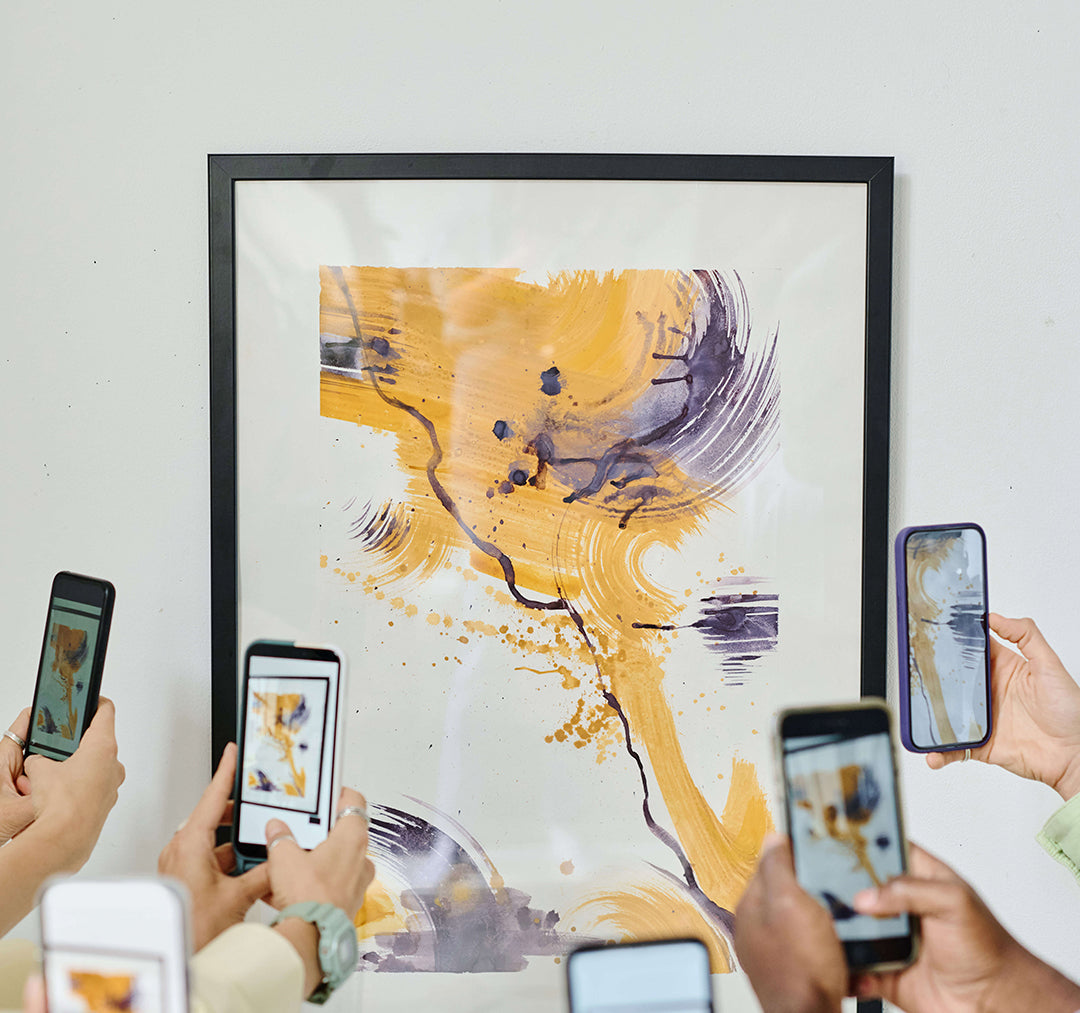 Group of people photographing a framed abstract artwork in yellow and purple hues with their smartphones at an art gallery.