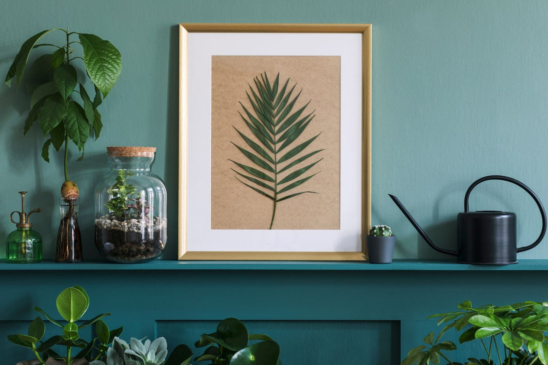 A framed leaf print with botanical elements against a teal backdrop 