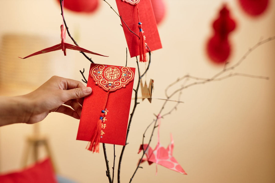 Hand placing a red envelope on decorative branches for Chinese New Year, symbolizing good luck, prosperity, and wealth in the home. 