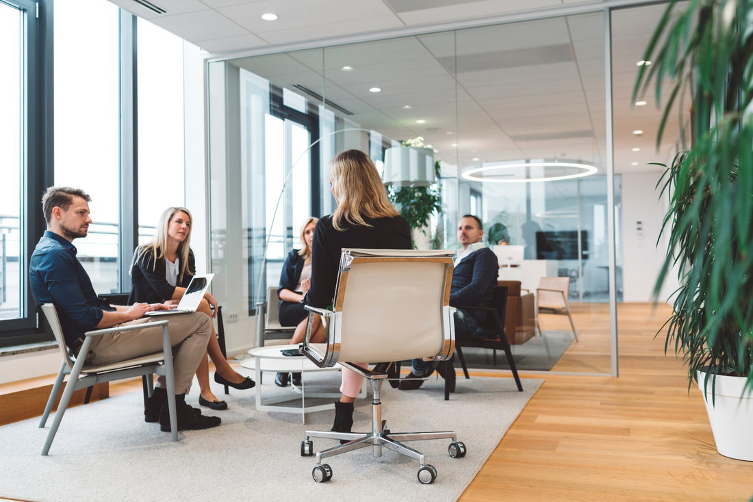 Modern office meeting with five professionals seated in a glass-walled conference space