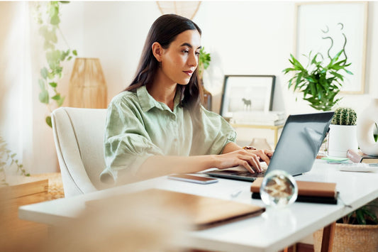 Woman working in a bright, plant-filled workspace demonstrating how to use Feng Shui art in a home office for focus and success.