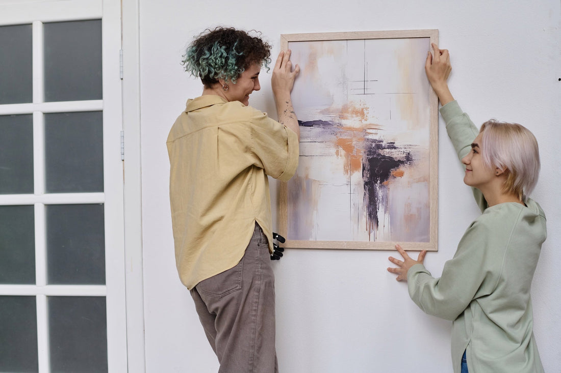 Two happy women hanging a framed artwork in their living room