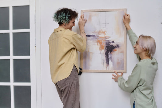 Two happy women hanging a framed artwork in their living room