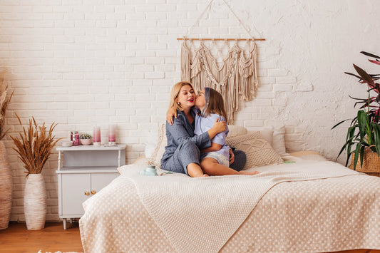Young daughter kissing her mother on the cheeks while they are seated on the bed.jpg