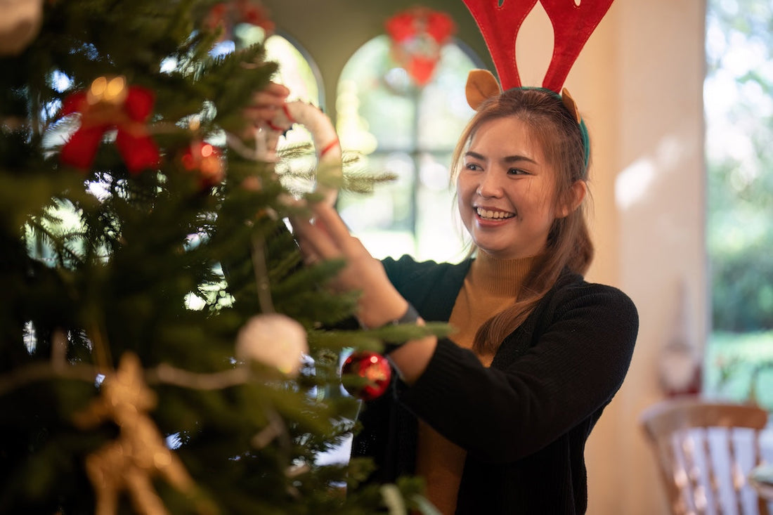 A woman with a reindeer headband decorating a Christmas tree
