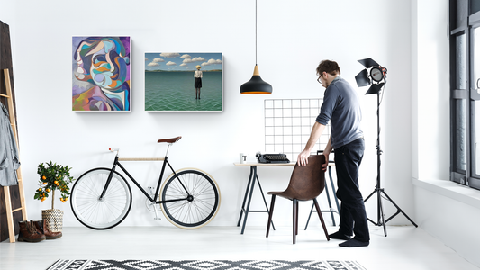 Man standing in a modern workspace with a bicycle, abstract modern and contemporary wall art, typewriter on desk, and stylish lighting, creating a creative studio vibe.