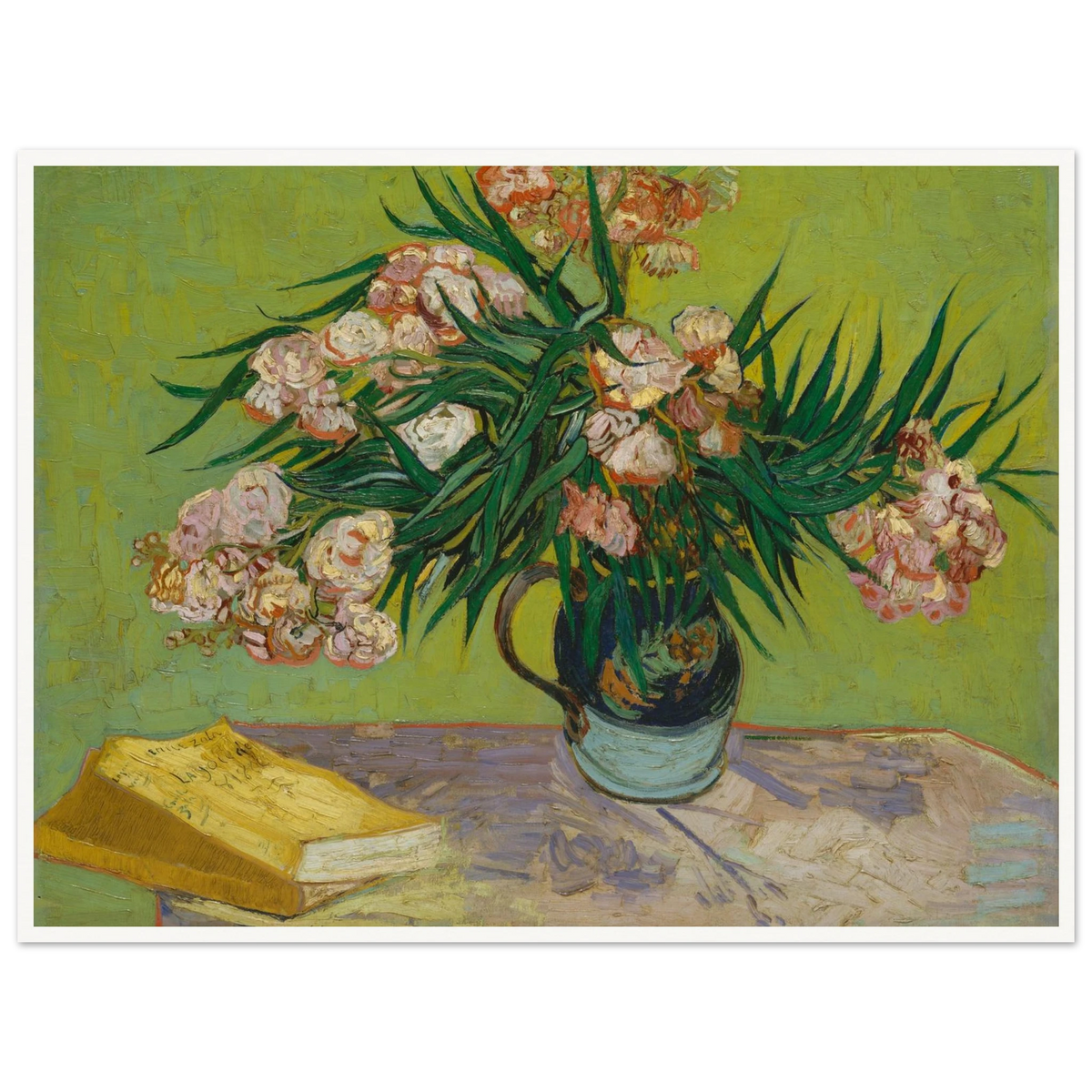 Pink oleanders bloom in a vase beside a yellow book on a green table.