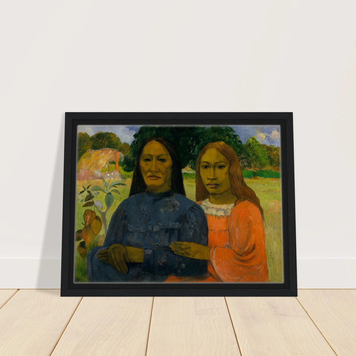 Two Tahitian women sit closely together in colorful dresses against a lush green landscape.