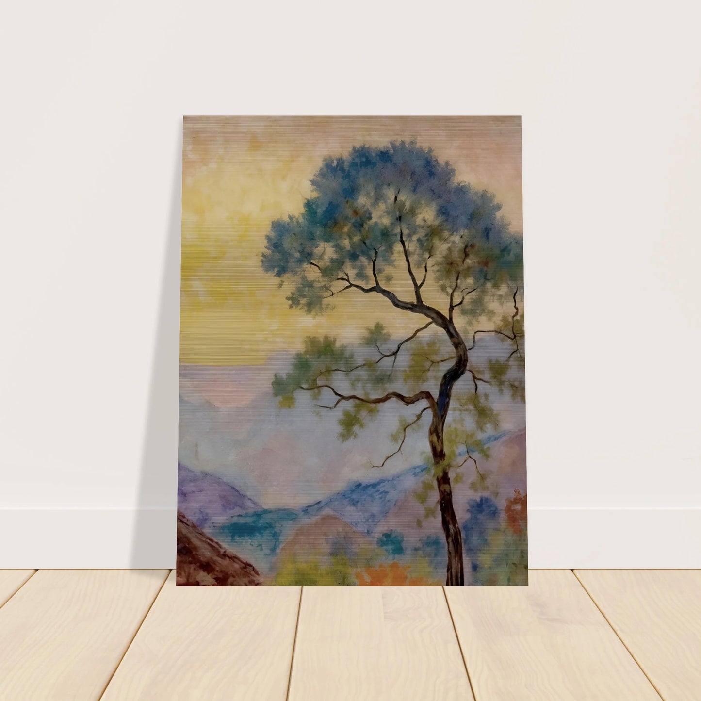 Delicate tree with green-blue foliage standing before pastel mountains under a soft yellow dawn sky.