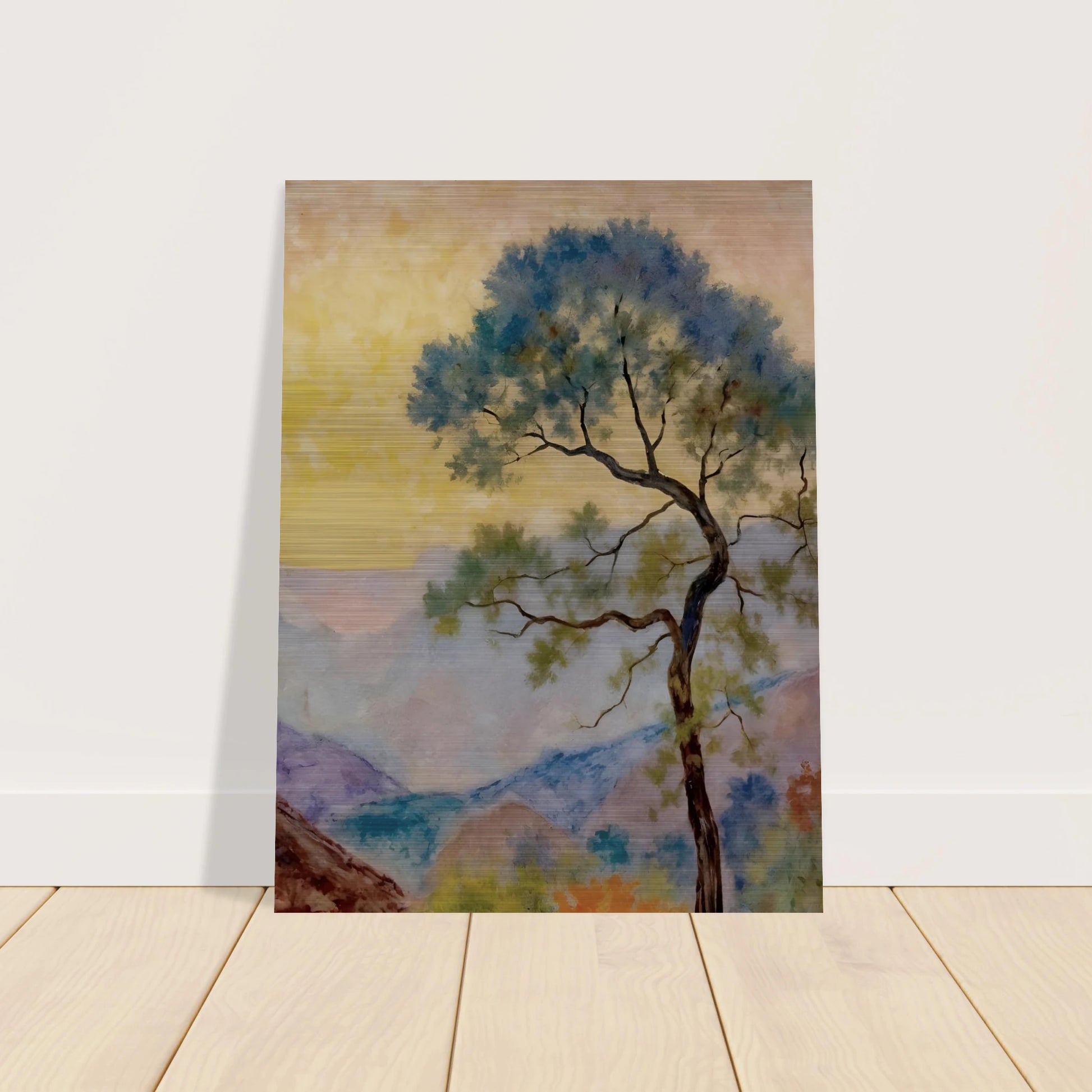 Delicate tree with green-blue foliage standing before pastel mountains under a soft yellow dawn sky.