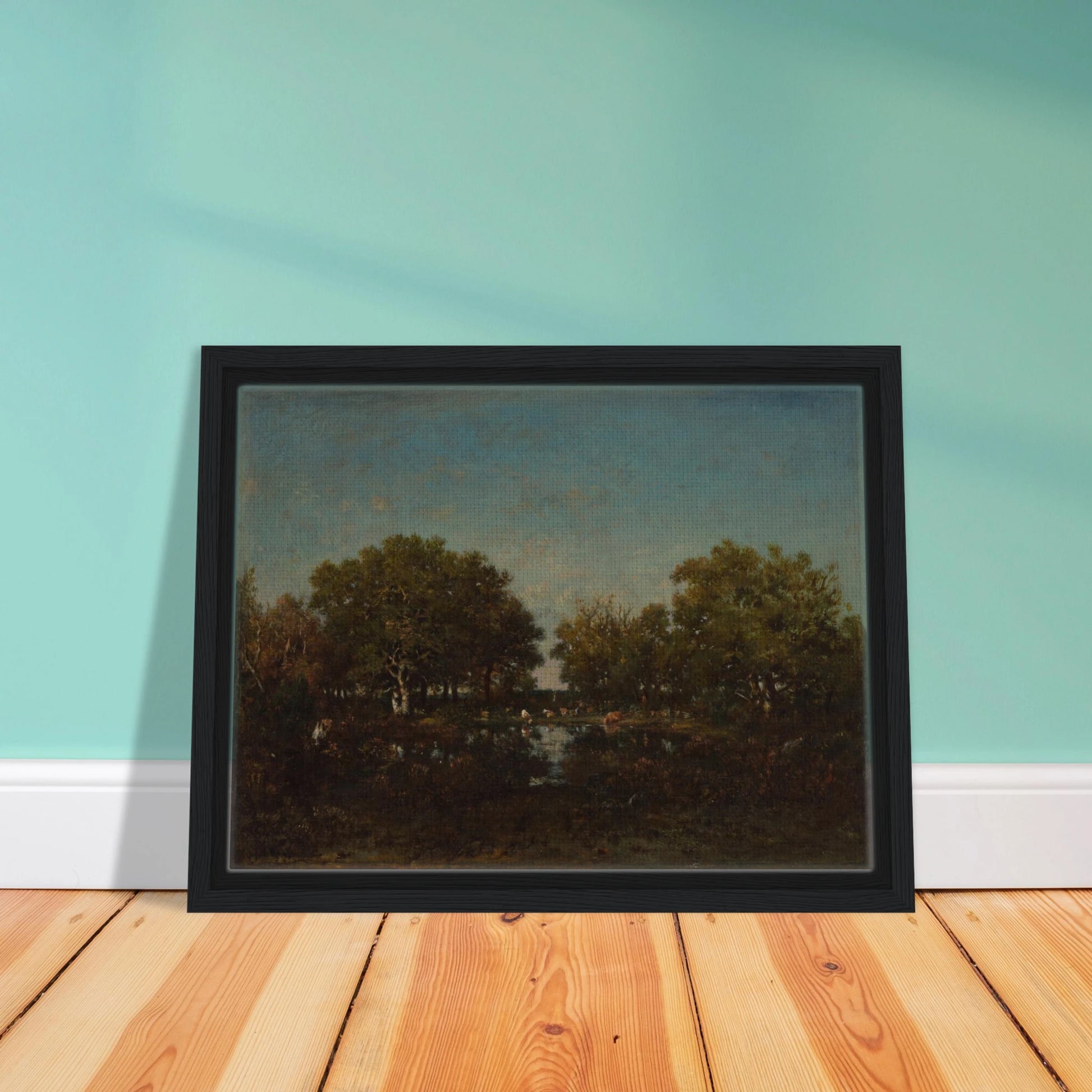 Cattle gather beside a reflective woodland pool beneath dense trees and a wide blue sky.