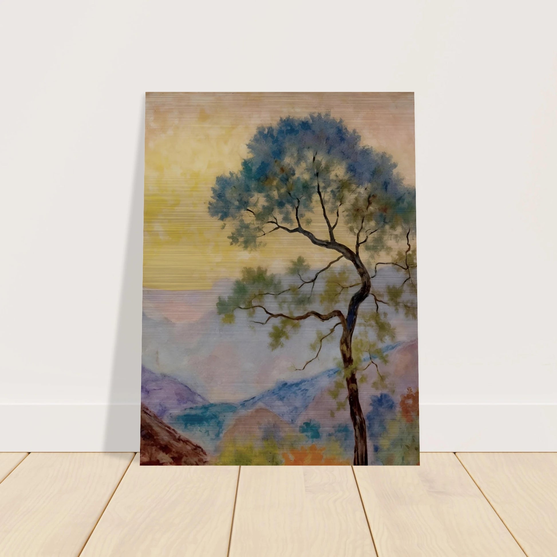 Delicate tree with green-blue foliage standing before pastel mountains under a soft yellow dawn sky.