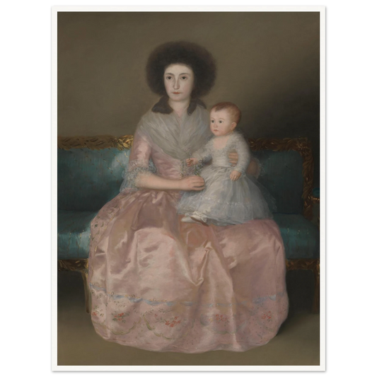 A seated woman in a pale pink gown holds a young child on a blue sofa against a muted background.
