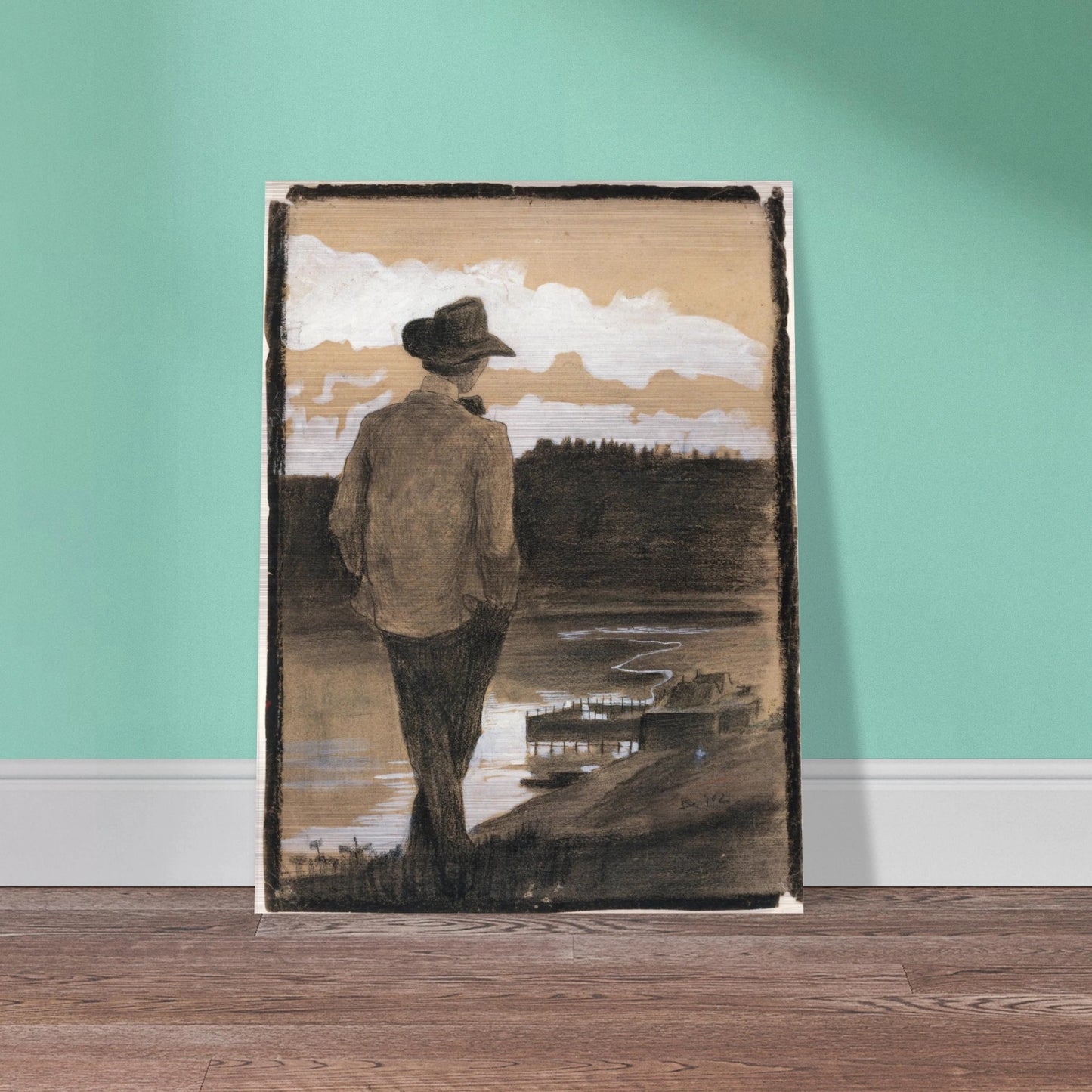 Young man in a hat stands by a riverbank, looking toward clouds and distant water