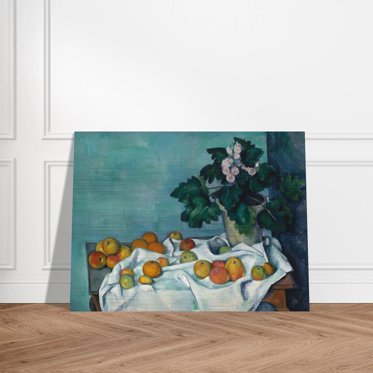 Apples on a white cloth beside a potted primrose plant against a blue-green wall.