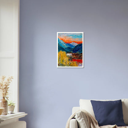 Snow-capped peaks rise above deep blue valleys and golden trees, beneath a fiery sunset glowing across the horizon.