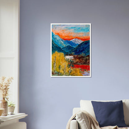 Snow-capped peaks rise above deep blue valleys and golden trees, beneath a fiery sunset glowing across the horizon.