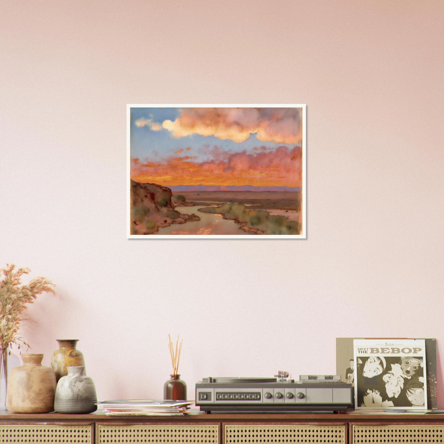 Soft desert river winding beneath glowing orange and pink sunset clouds, with distant plains and muted cliffs in a serene landscape.