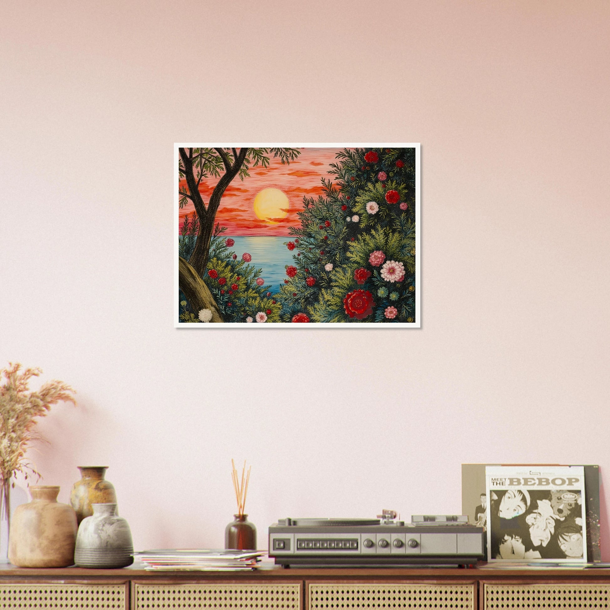 A vivid sunset over the ocean framed by lush bushes filled with red, pink, and white flowers.