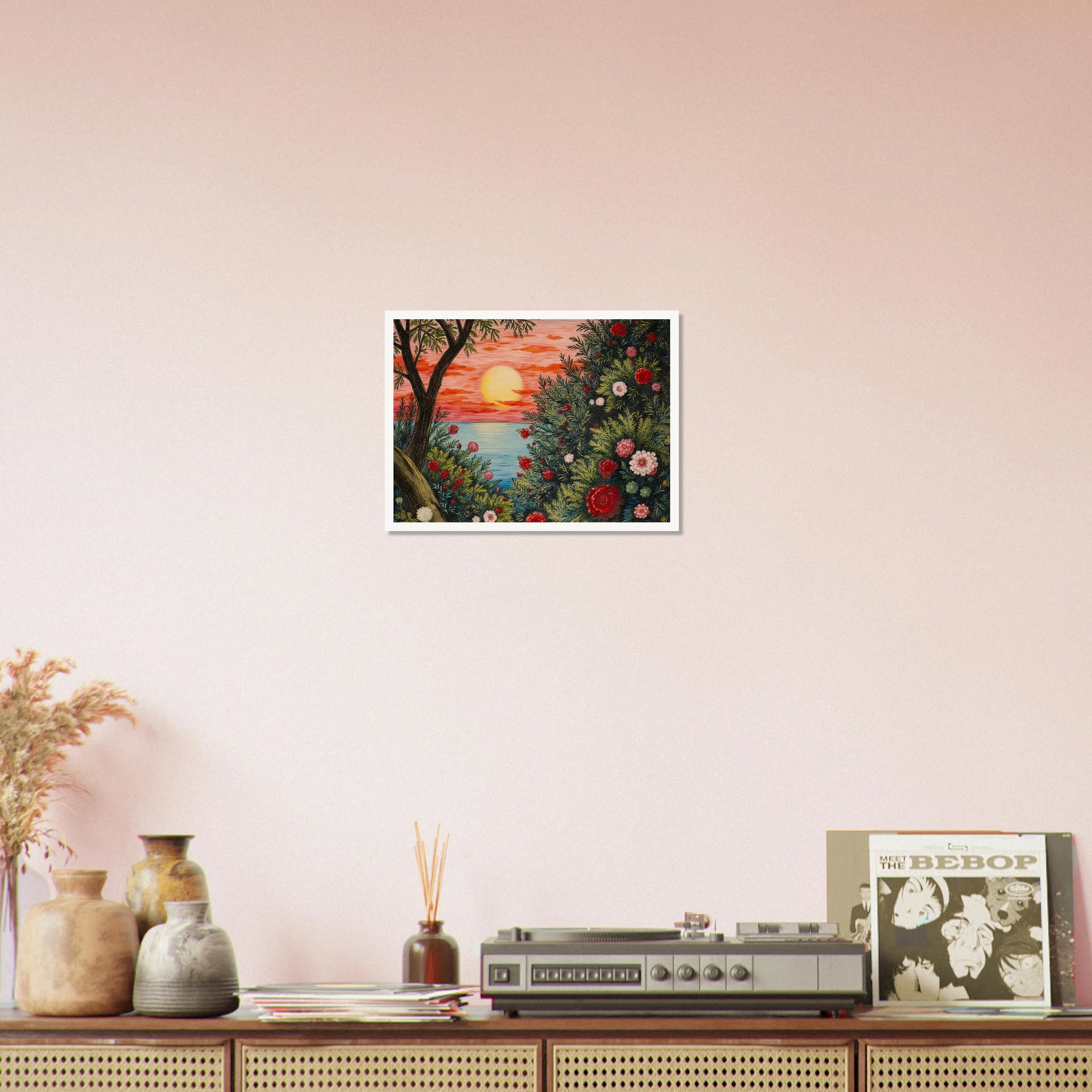 A vivid sunset over the ocean framed by lush bushes filled with red, pink, and white flowers.