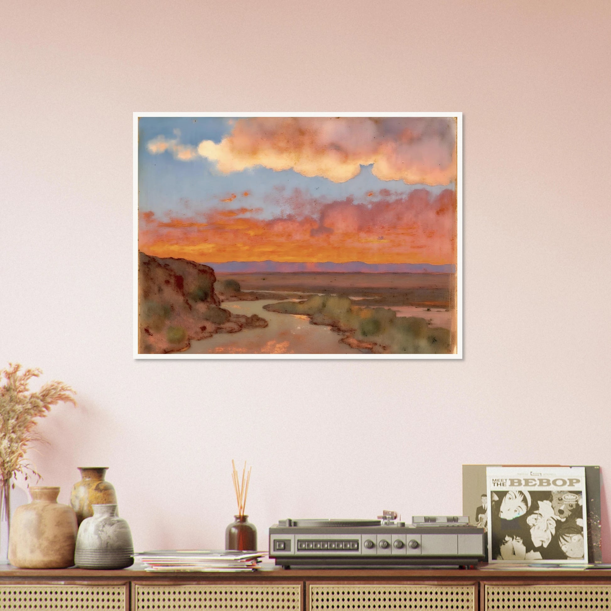Soft desert river winding beneath glowing orange and pink sunset clouds, with distant plains and muted cliffs in a serene landscape.