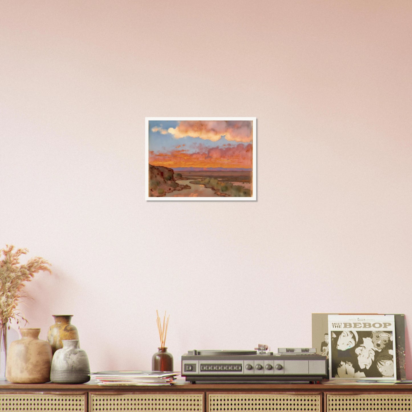 Soft desert river winding beneath glowing orange and pink sunset clouds, with distant plains and muted cliffs in a serene landscape.