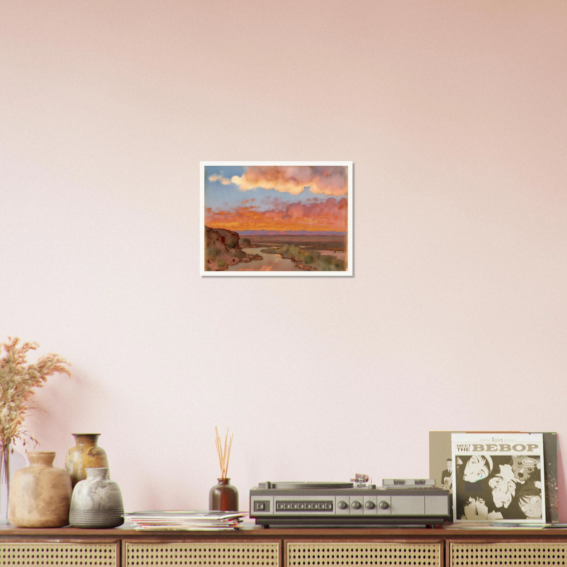 Soft desert river winding beneath glowing orange and pink sunset clouds, with distant plains and muted cliffs in a serene landscape.