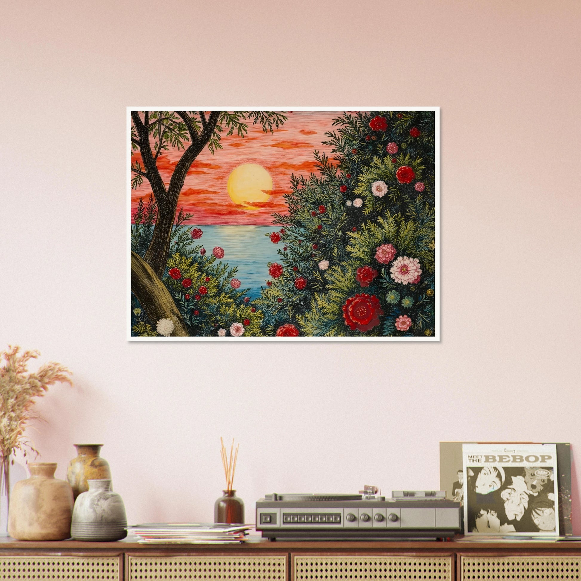 A vivid sunset over the ocean framed by lush bushes filled with red, pink, and white flowers.