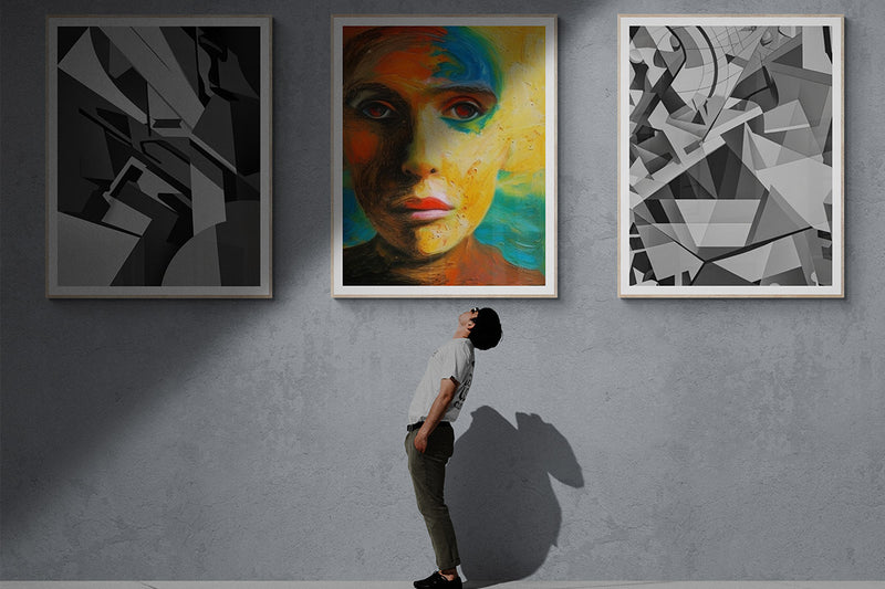 A young man standing and looking up at a gallery wall displaying three artworks, including two monochrome abstracts and one colorful portrait.