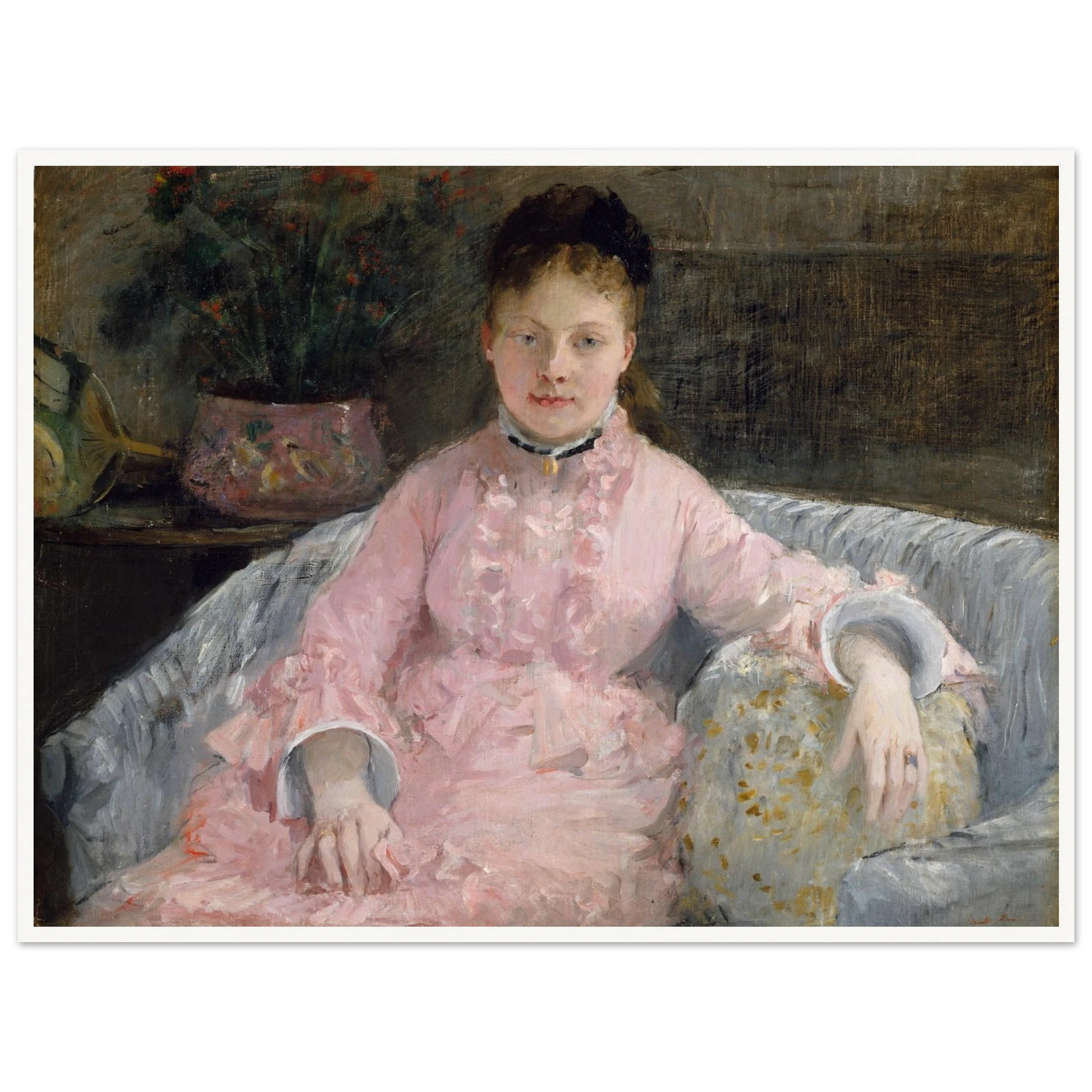 Young woman in a pink dress sits on a sofa beside flowers and a patterned pillow