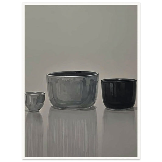 Still life of three ceramic bowls in shades of gray and black, displayed against a neutral background with reflections on a smooth surface.