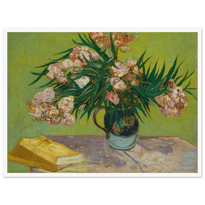 Pink oleanders bloom in a vase beside a yellow book on a green table.
