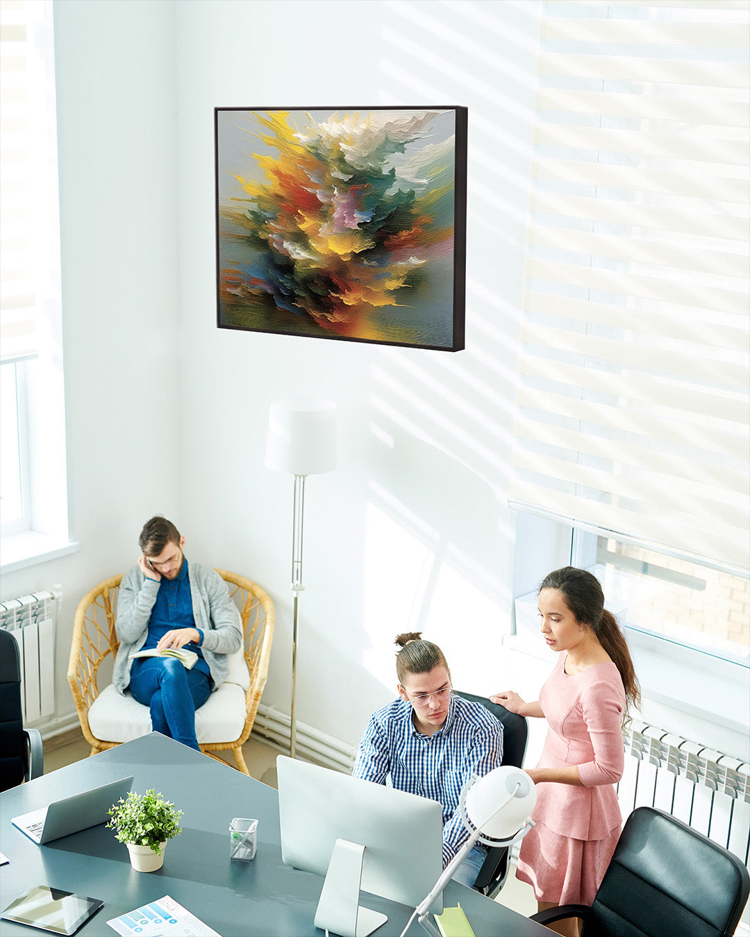 Photo of an office with people working. A vibrant, colorful abstract painting is on the white wall between two windows. 